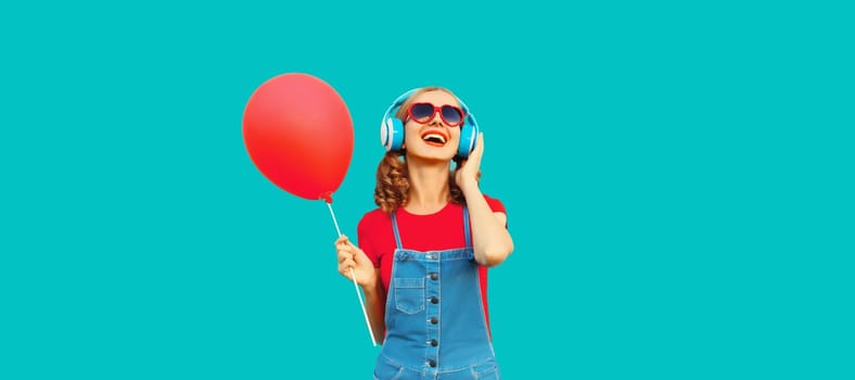 Happy cheerful young woman in wireless headphones listening to music with red balloon on blue studio background