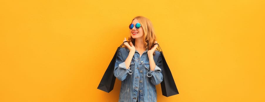 Stylish beautiful happy smiling young woman posing with black shopping bags on yellow studio background