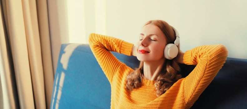 Happy relaxed young woman listening to music with wireless headphones with closed eyes lies on the couch at home