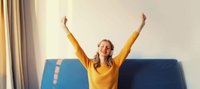 Happy cheerful young woman listening to music with headphones having fun sitting on sofa at home