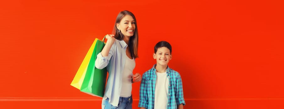 Happy smiling mother and son child together with shopping bags on red wall background