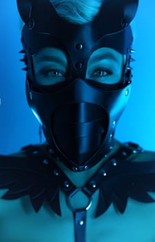 portrait of a hot sexy girl in a leather cat mask and muzzled in bdsm handcuffs on neon blue light background