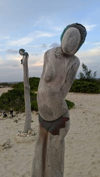 Abstract wooden figure on sandy beach, weathered texture signifies solitude and time's passage, serene coastal ambiance