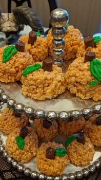 Miniature pumpkin marshmallow treats on decorative stand, with blurred skull in background, for a Halloween autumn gathering.