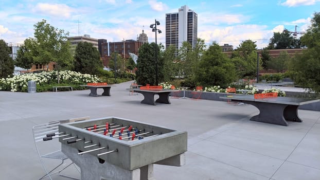 Urban park in Fort Wayne, Indiana featuring modern recreation facilities including concrete table football and ping pong tables amidst lush greenery, symbolizing city leisure and planning, 2021.