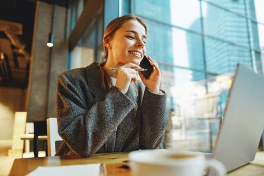 Smiling woman manager talking with client and work on laptop in cafe. Distance work concept