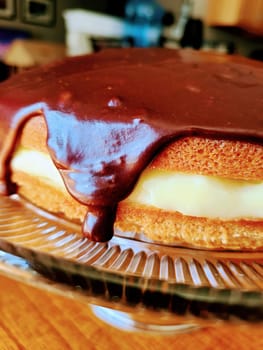 Freshly baked layered sponge cake, glazed in glossy chocolate, displayed on elegant glass stand in homey Fort Wayne kitchen, Indiana - A Mark Klein creation, 2022