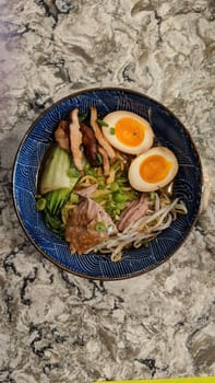 Overhead view of colorful ramen bowl with diverse toppings on granite countertop, showcasing Japanese cuisine and gourmet dining