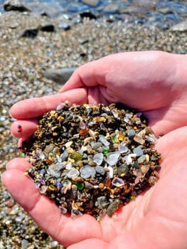 Hand Holding Sea Glass and Pebbles at Glass Beach, California 2022 - A Close-up of Beachcombing Treasures Against a Coastal Backdrop