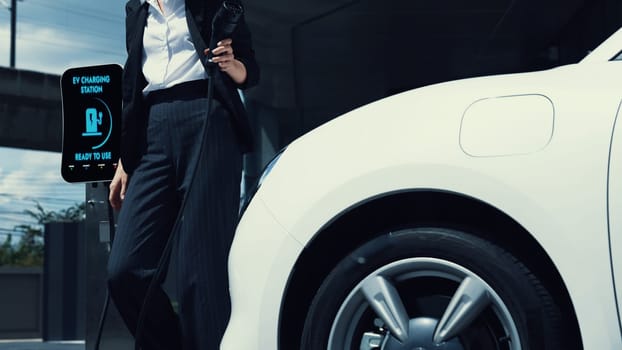 Businesswoman recharge her electric car from charging station at city center or public parking car. Eco friendly rechargeable car using alternative clean energy. Peruse