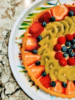 Freshly baked fruit tart with vibrant strawberries, kiwi, and blueberries on a marble countertop in a sunny Indiana kitchen, 2022