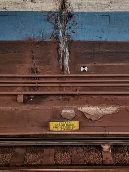 Urban Decay and Safety in New York City Train Station, 2022 - Close-up of Weathered Railway Tracks, Platform Edge, and Warning Sign