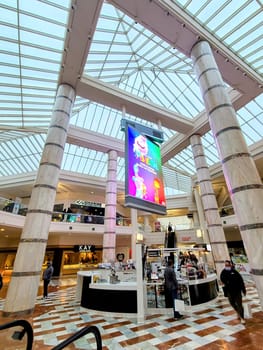 Shoppers engage at a modern kiosk in a sunlit, luxurious San Francisco mall, surrounded by marble pillars and digital advertising, 2023