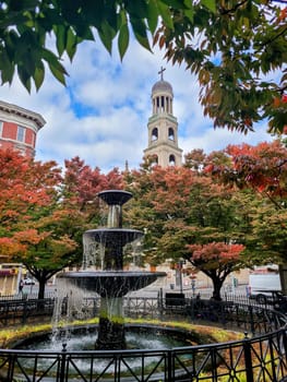 Autumn in Greenwich Village, New York City, featuring a lively fountain, fall-colored trees, and a historic church tower in the backdrop
