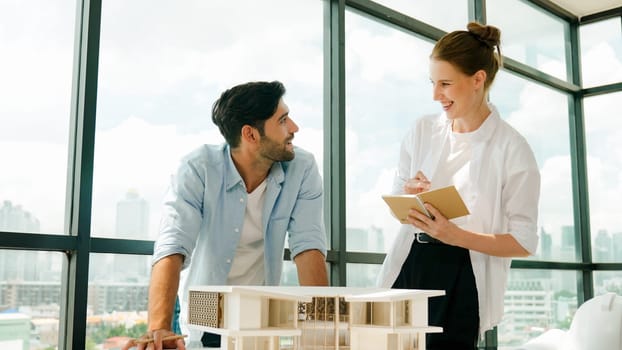 Skilled architect engineer team discussion about house model construction. Smart interior designer sharing, talking about building design while beautiful coworker taking a note. Design. Tracery