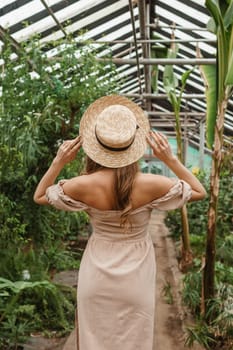 A beautiful young woman takes care of plants in a greenhouse. The view from the back. Concept of gardening and an eco-friendly lifestyle.