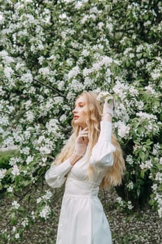 A blonde girl with long hair on a walk in a spring park. Springtime and blooming apple trees