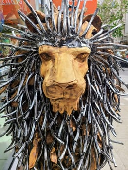 Eye-level perspective of a detailed lion's head sculpture with a spiked metallic mane, set against an urban city backdrop in San Francisco, 2023, illustrating themes of power and majesty.