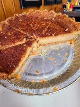 Close-up of half-eaten sugar cream pie in disposable dish on wooden surface, conveying homey comfort food in a casual Huntington, Indiana restaurant, 2023