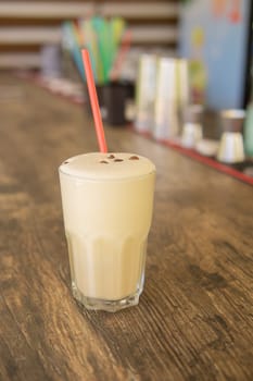 A cold coffee cocktail in a clear glass with a straw on a wooden bar counter.