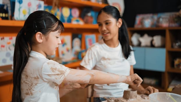 Diverse highschool student modeling cup of clay while wearing dirty shirt at art lesson. Multicultural student working or making dough art in creative activity. Blurring background.. Edification.