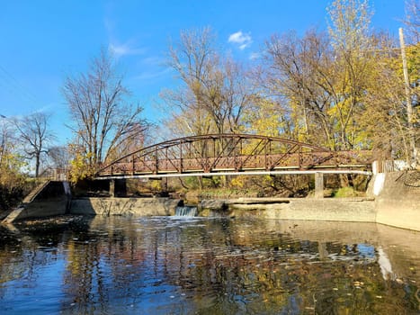 Tranquil autumn scene of a rustic metal bridge over a serene creek, framed by leafy trees in Fort Wayne, Indiana - 2022