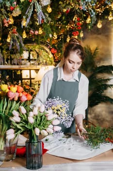 A woman in her florist shop collects bouquets of flowers. The concept of a small business. Bouquets of tulips for the holiday on March 8