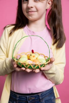 Beautiful small girl with bunny ears holding an egg basket for easter festivity, posing with pretty spring trinkets. Happy and energetic child celebrating the festive season in the studio.