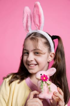 Sweet little girl posing with a cute pink stuffed rabbit on camera, showing her easter themed toys and decorations. Small child with bunny ears feeling happy and excited about celebration.