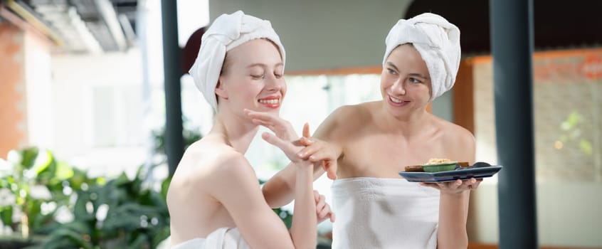 Portrait of two attractive woman in towel giggling during hold the herbal bowl surrounded by natural spa environment. Pretty girls with beautiful skin using herbal scrub at spa salon.Tranquility.