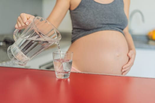 Embracing the vital benefits of water during pregnancy, a pregnant woman stands in the kitchen with a glass, highlighting hydration's crucial role in maternal well-being.