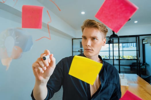 Professional caucasian businessman writing marketing idea by using mind map and sticky notes on glass board at modern meeting room. Creative business and planing concept. Closeup. Immaculate.