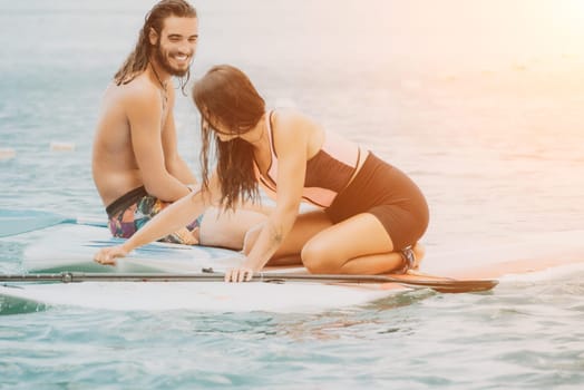 Sea woman and man on sup. Silhouette of happy young woman and man, surfing on SUP board, confident paddling through water surface. Idyllic sunset. Active lifestyle at sea or river