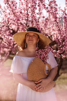 Woman blooming peach orchard. Against the backdrop of a picturesque peach orchard, a woman in a long white dress and hat enjoys a peaceful walk in the park, surrounded by the beauty of nature