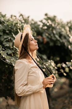 Woman with straw hat stands in front of vineyard. She is wearing a light dress and posing for a photo. Travel concept to different countries.