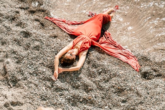 Woman red dress sea. Female dancer in a long red dress posing on a beach with rocks on sunny day.