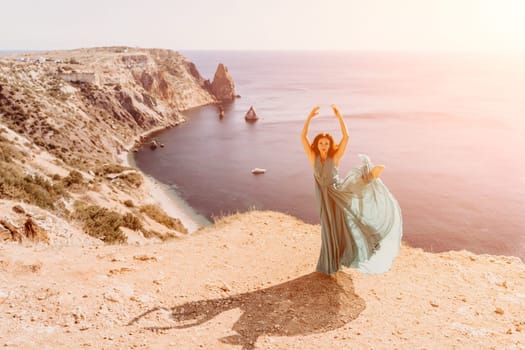 Woman green dress sea. Female dancer posing on a rocky outcrop high above the sea. Girl on the nature on blue sky background. Fashion photo