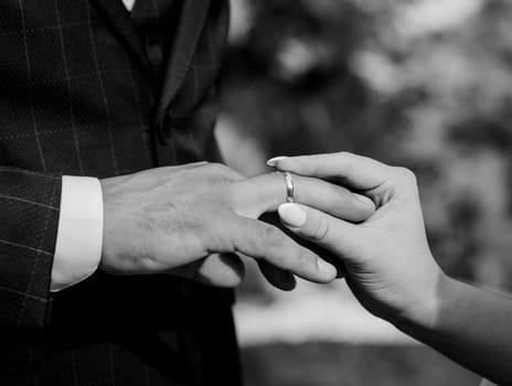 Couple exchanging wedding rings during their wedding ceremony. Cropped shot of groom putting a wedding ring. Black and white image