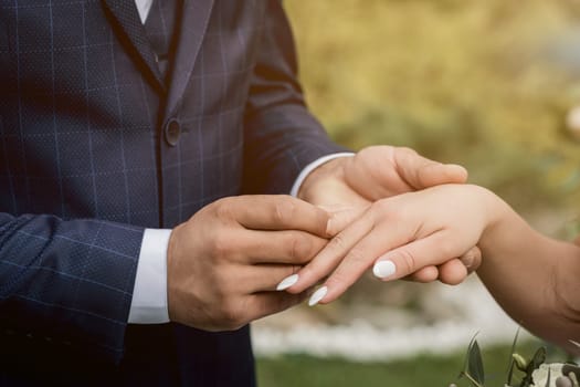 couple exchanging wedding rings during their wedding ceremony outdoors. Cropped shot of groom putting a wedding ring on the finger of the bride.