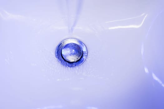 stream of clean water flows into in blue tones. Sink plug hole close up macro.