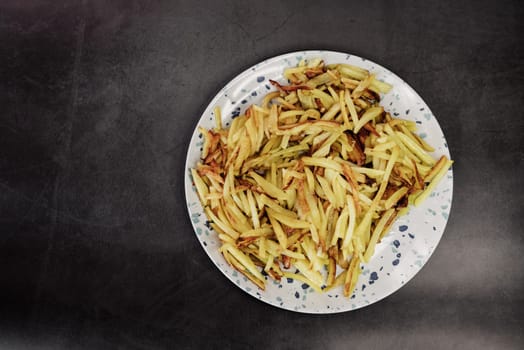 golden fried potatoes in a plate on a dark background with a copy space