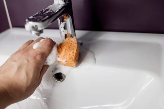 Male hand with sponge cleaning faucet. cleaning of the bathroom