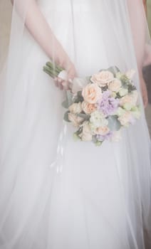 Beautiful wedding bouquet of flowers under veil in the hands of the bride