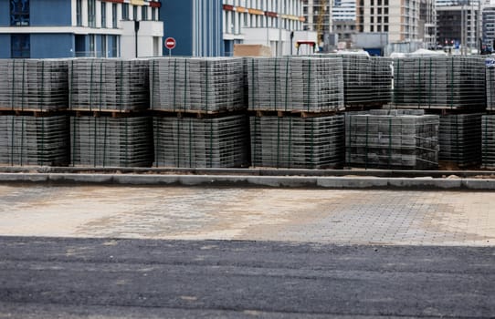 tiles, made of concrete, are designed to repair the sidewalk and are stacked on wooden pallets that stand near the sidewalk