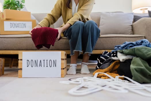 Young Asian women sit in living room sorting clothes for donation in a donation box second hand clothes. Donate concept.