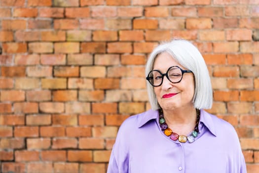 portrait of beautiful senior woman in glasses winking looking at camera, concept of happiness of elderly people and active lifestyle, copy space for text