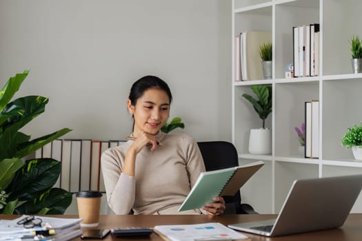 woman taking note in notebook while using laptop at home. business woman writing plan on book while working on laptop in living room.