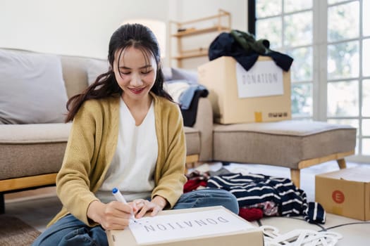 Young woman write donation box second hand in the living room. Donation Concept.