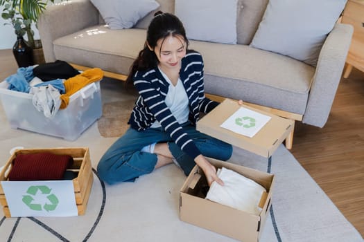 Young Asian women sit in living room sorting clothes for donation and recycle for reuse. Donate concept.