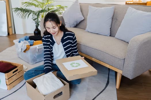 Young Asian women sit in living room sorting clothes for donation and recycle for reuse. Donate concept.